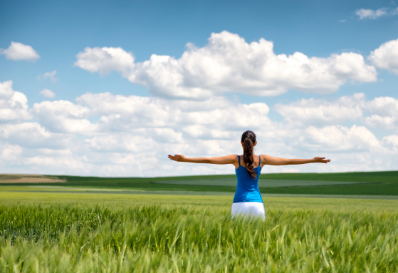 Image of a girl in a wheat field standing in the distance with her back to the camera and her arms o